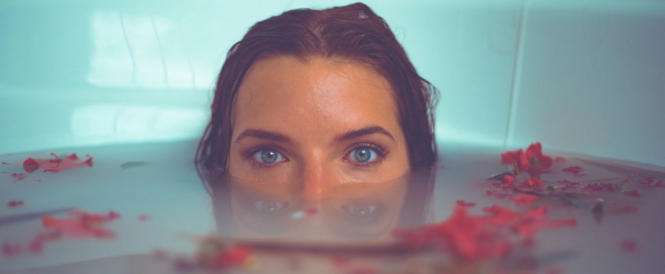 woman with half her face submerged in a bath with rose petals