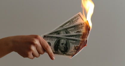hand holding burning U.S. Dollar bills