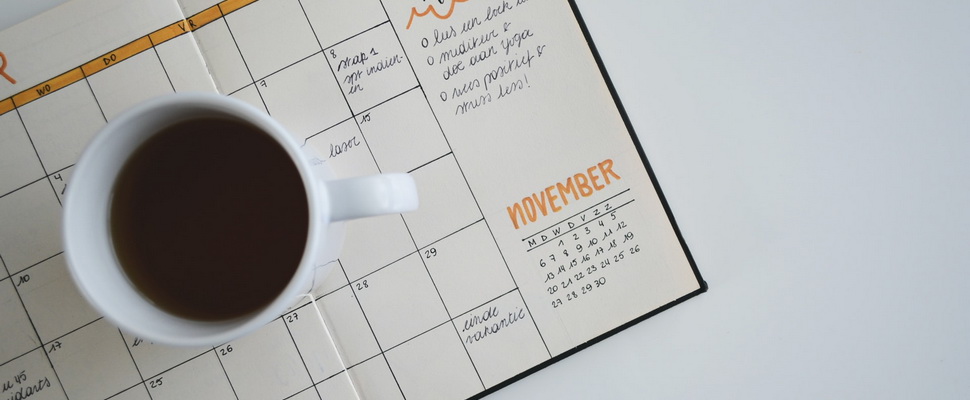 monthly planner and a mug of coffee on a white table