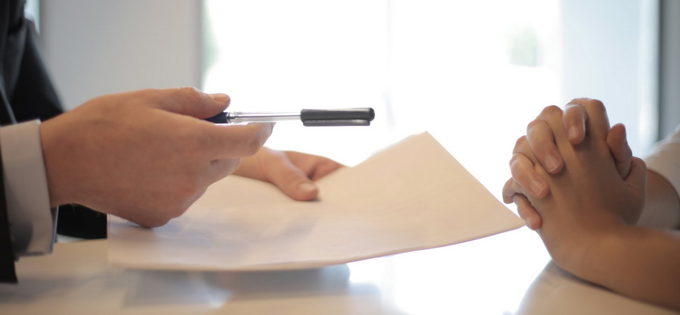 one person handing pen and paper to another person over a desk
