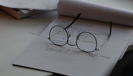 notepad on desk with technical requirement notes and graphs on it, with spectacles lying on top